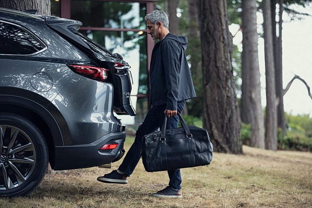 man holding luggage opening rear liftgate of 2020 mazda cx-9 by swiping his foot underneath the bumper